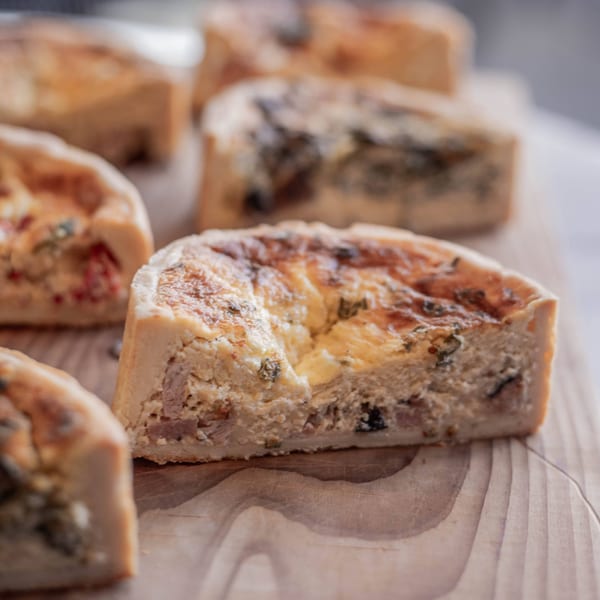 Several savory quiche slices with golden crusts and creamy fillings on a wooden board.
