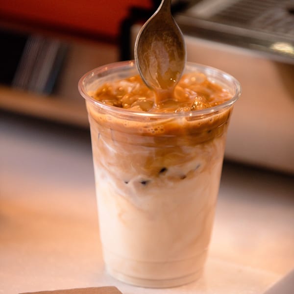 A spoon stirs a creamy, iced coffee drink in a clear plastic cup at Tortoni Caffe.