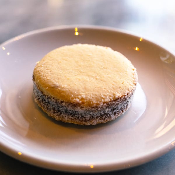 A round alfajor cookie with dulce de leche and shredded coconut on a white plate.