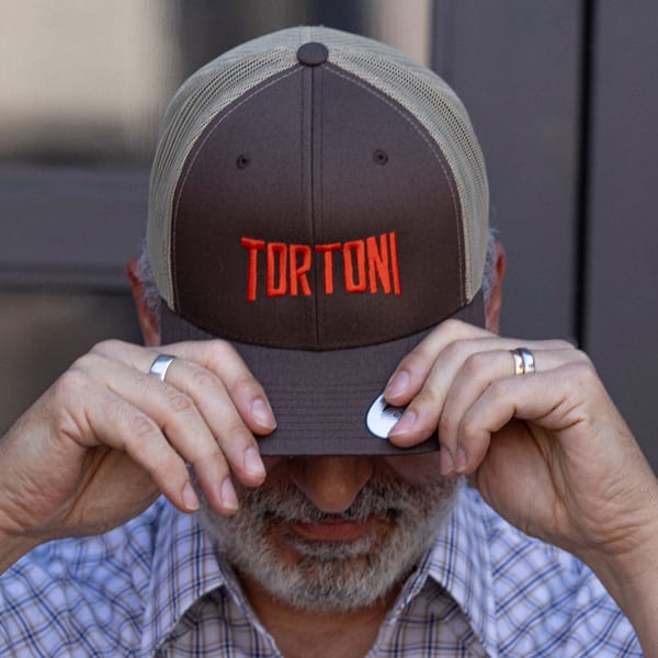 A man wearing a brown Tortoni Caffe hat with red lettering, pulled down over his eyes.