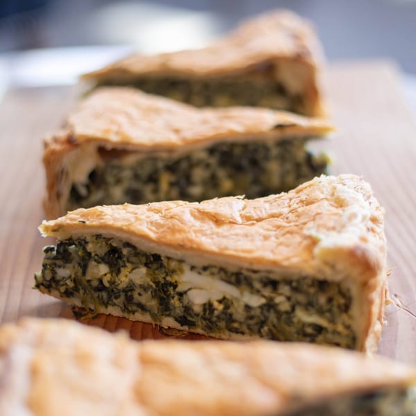 Close-up of several slices of savory spinach and cheese pie on a wooden board at Tortoni Caffe.